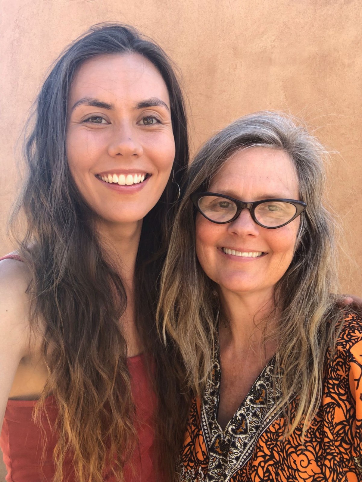 Ana Cortez and her daughter Naga smiling in front of an adobe wall